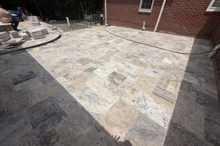 Silver travertine hardscape installation in progress at brick home — Garrison Landscaping