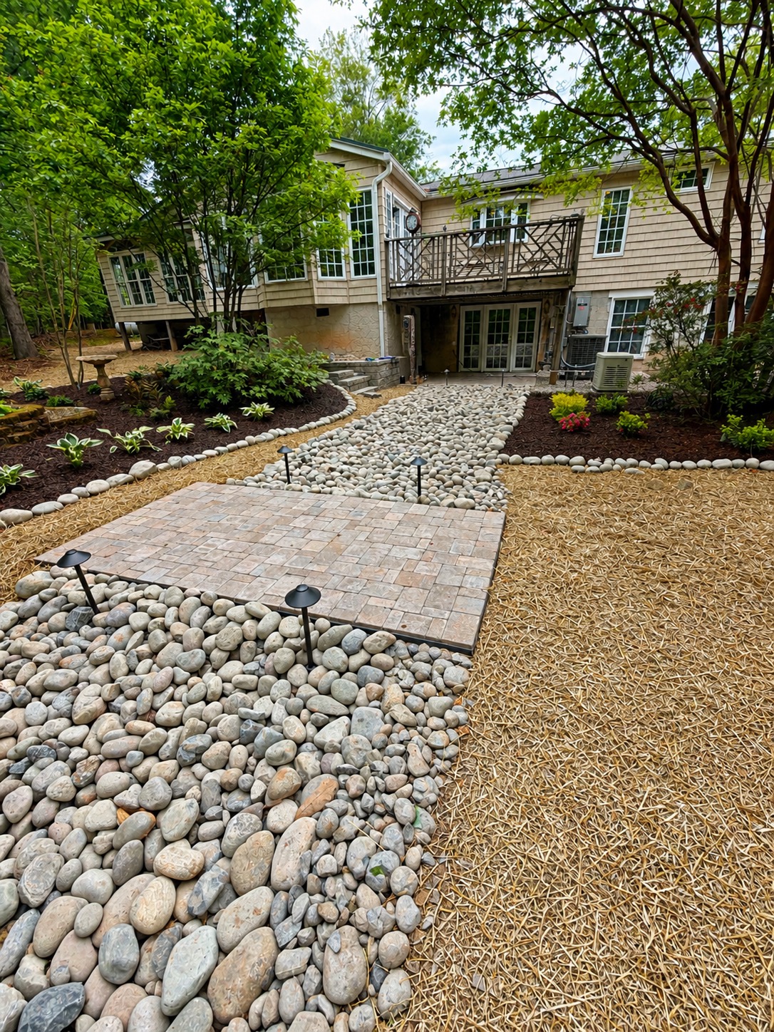 Custom landscape design with river-rock dry creek, paver landing, hostas, and pine straw — Garrison Landscaping