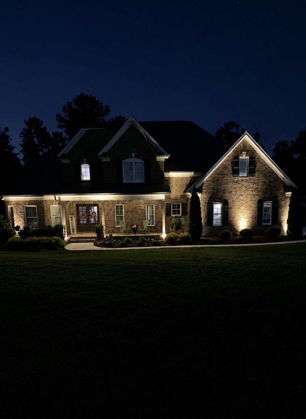 Warm LED landscape uplighting on brick facade and porch at night — Garrison Landscaping