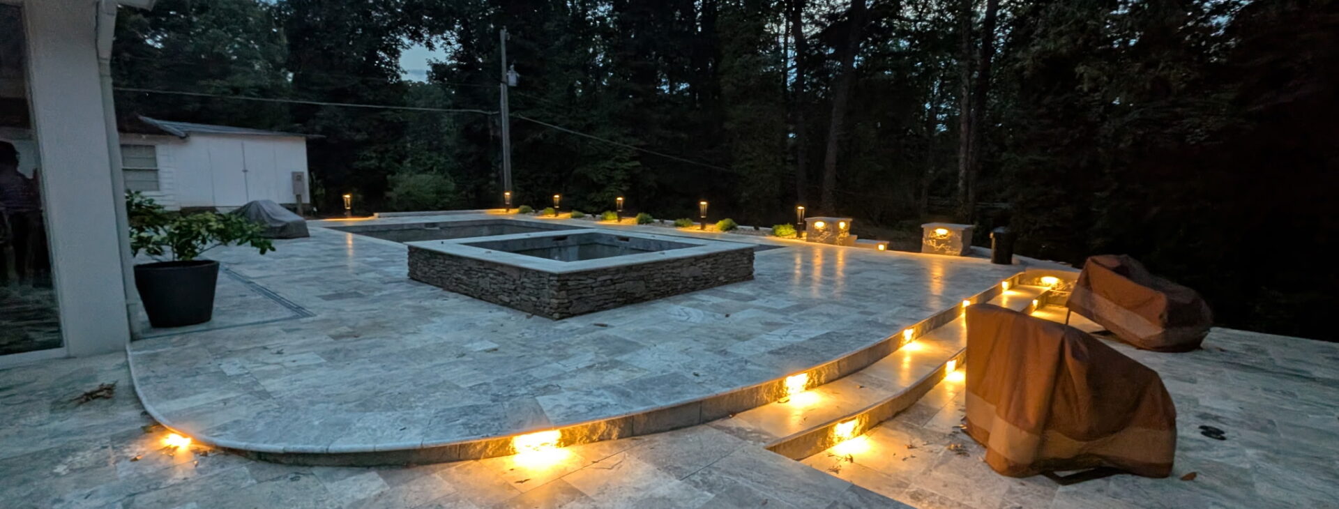 Recessed landscape lighting along travertine pool patio steps illuminating the path at dusk