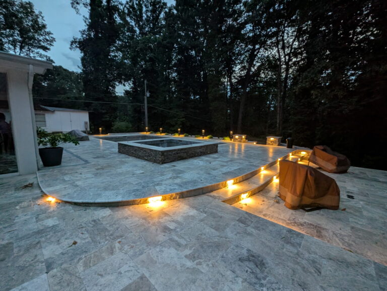 Recessed landscape lighting along travertine pool patio steps illuminating the path at dusk