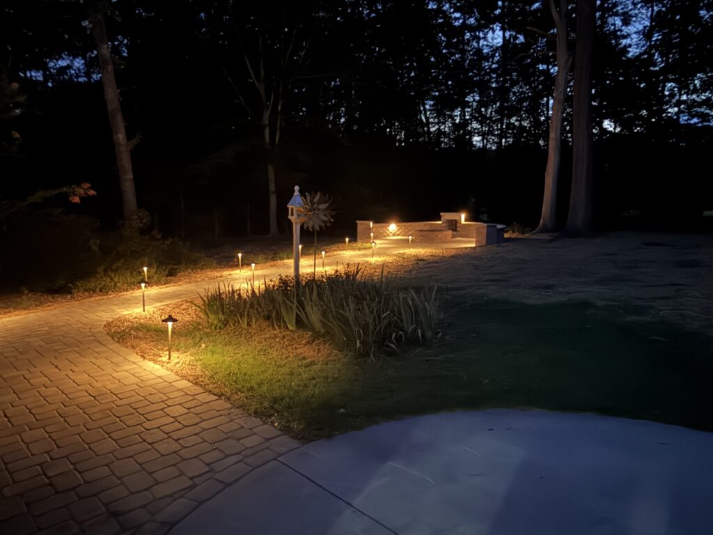 Landscape Lighting Guide: How to Light Your Home and Outdoor Living Spaces 5 Path lights lining a curved paver walkway leading to a stone fire pit patio at dusk