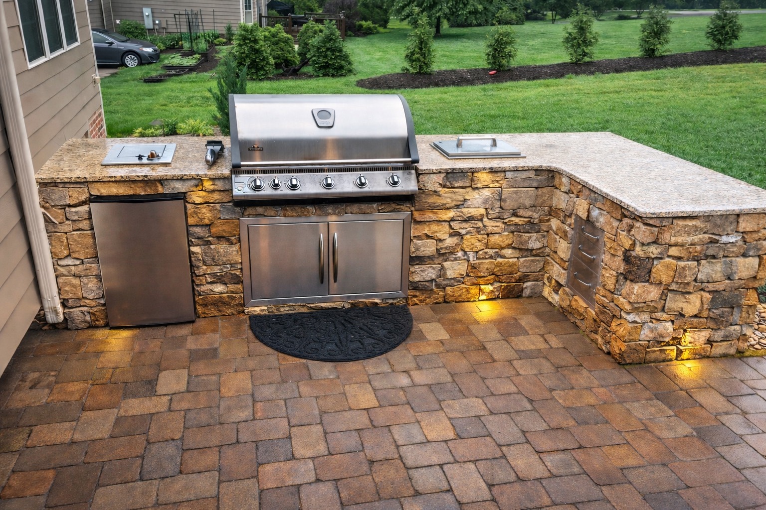 Custom stone-clad outdoor kitchen with stainless grill and side burner — Garrison Landscaping