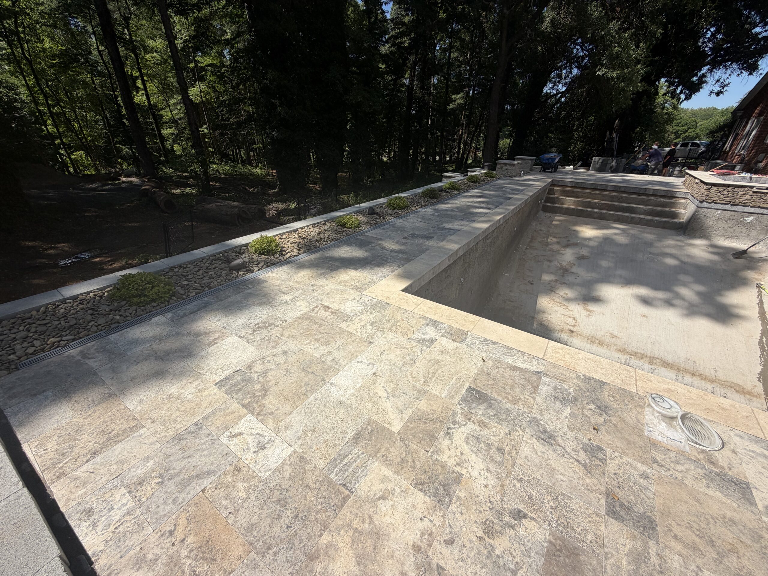 Silver travertine pool deck with retaining wall and drainage strip — Garrison Landscaping
