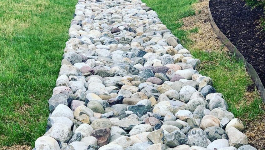 Multicolor river rock dry creek bed running through a backyard lawn