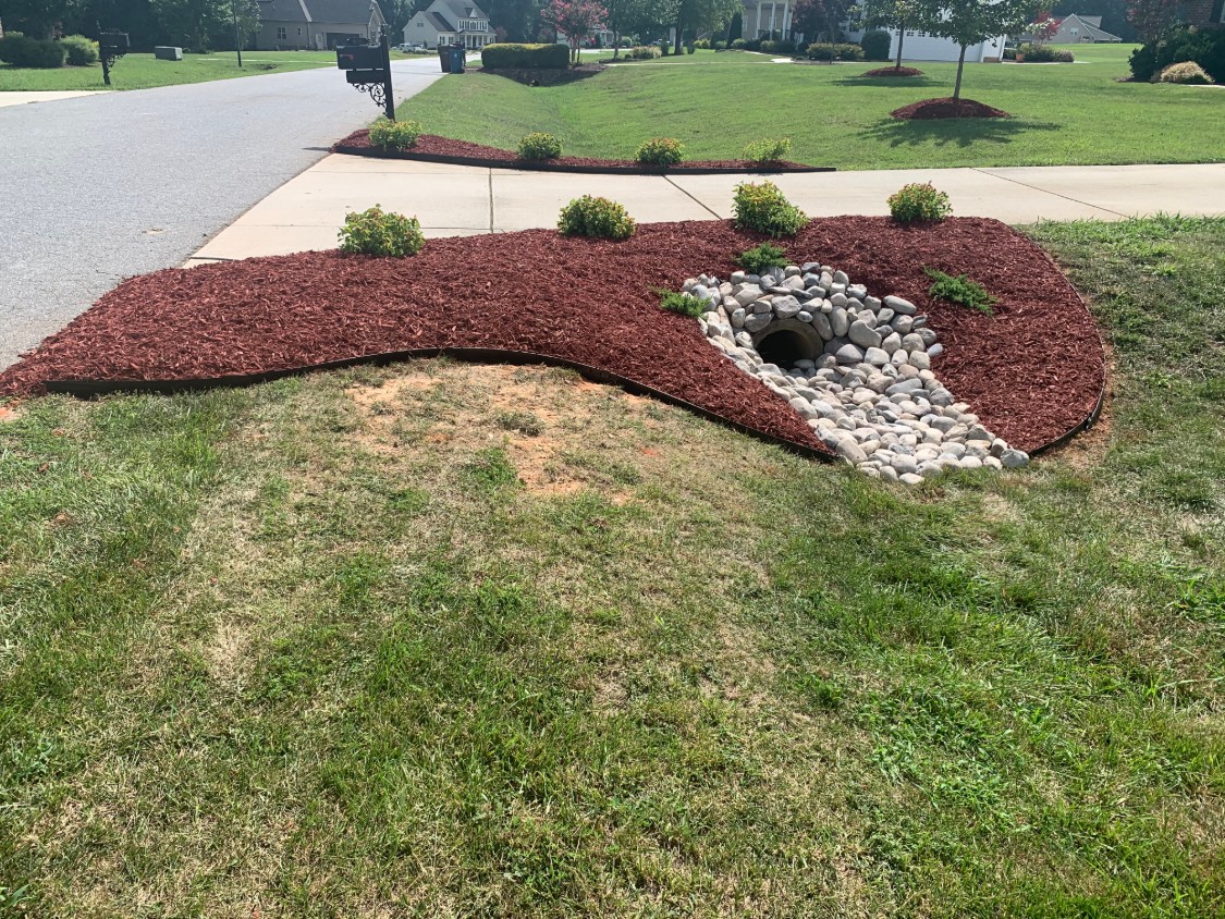 Driveway culvert finished with river rock inside a landscaped mulch bed