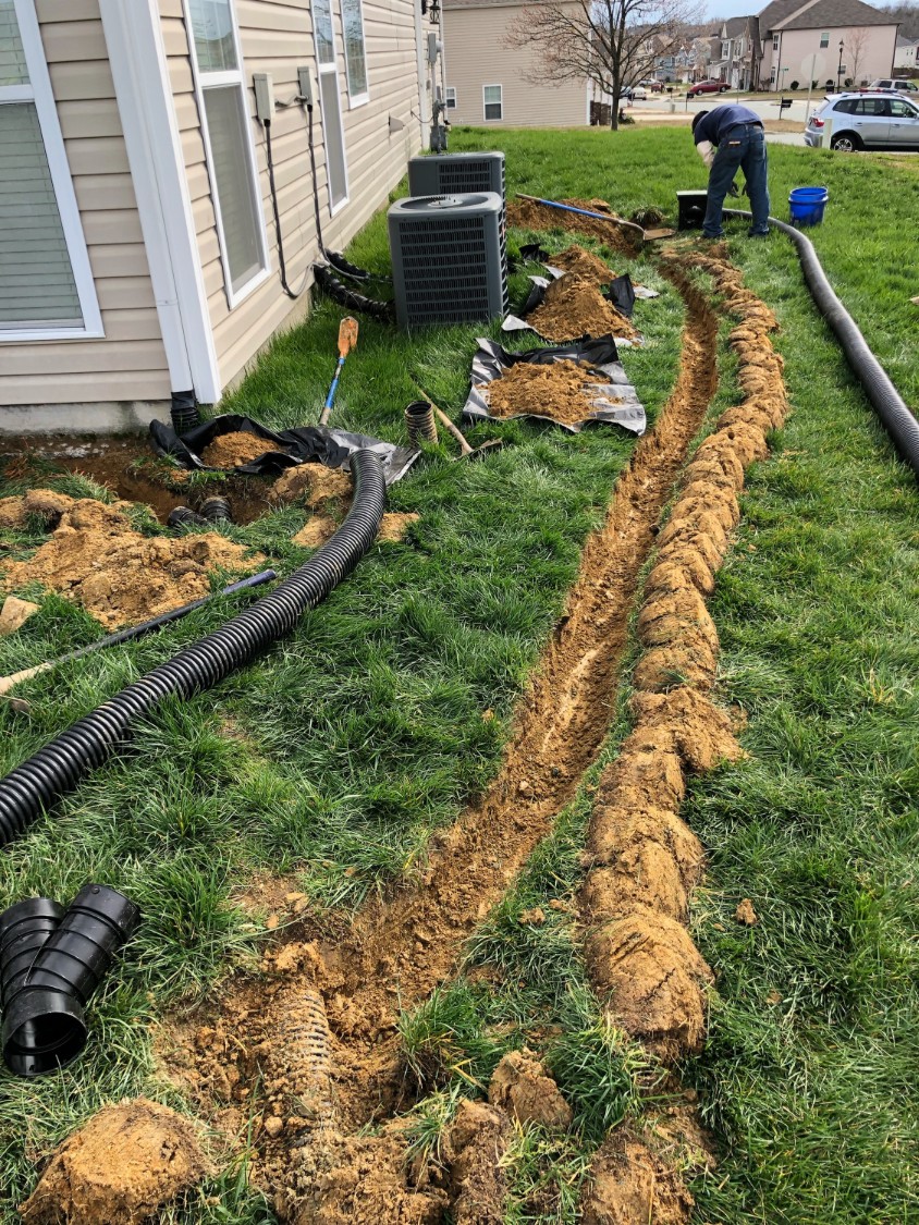 Crew installing underground downspout drain lines beside a home