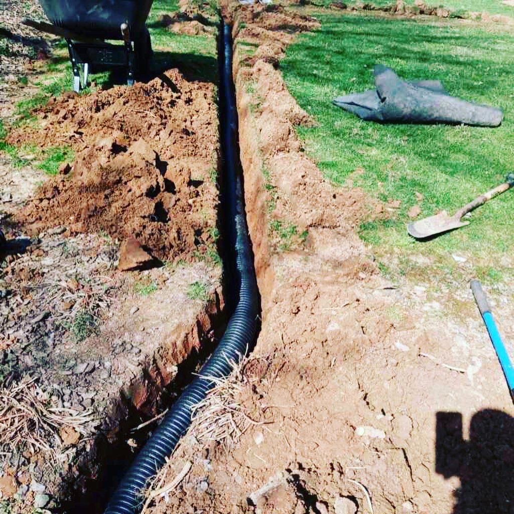 Corrugated drain pipe laid in a freshly dug trench in red clay