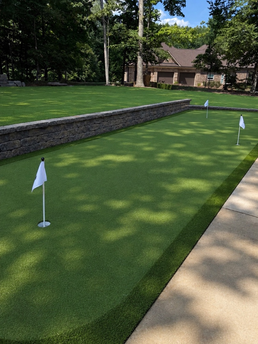 Finished backyard synthetic putting green with flags, fringe collar and a stone block wall