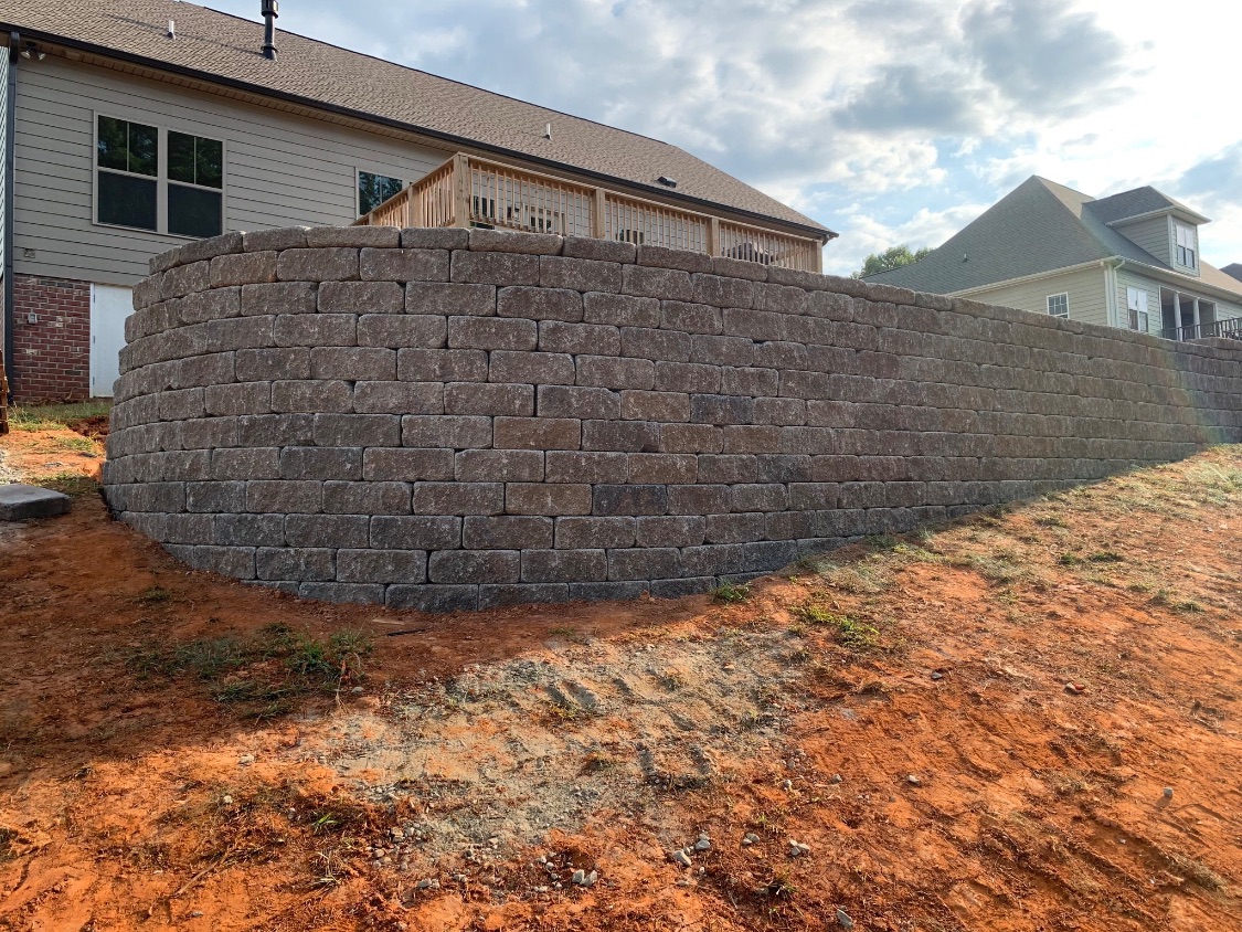 Tall curved segmental block retaining wall supporting a backyard grade behind a new home