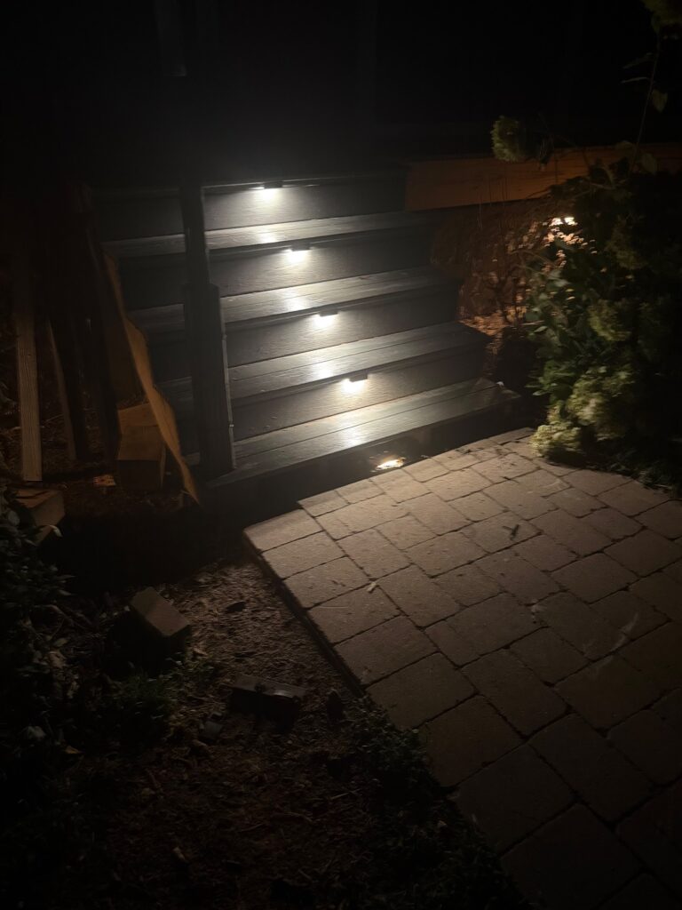 Custom Outdoor Steps & Stairways in Guilford, Rockingham and Surrounding Counties 6 Wooden deck steps with riser lights at night above a paver landing