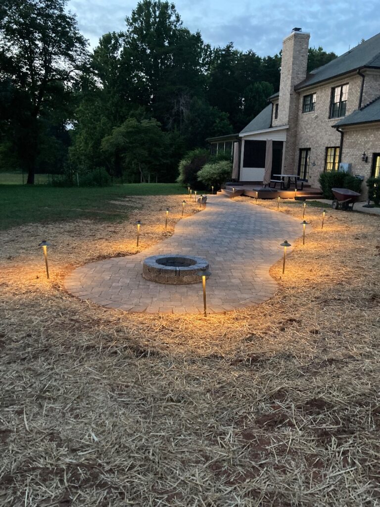 Paver fire pit patio at dusk lined with landscape path lights leading to the back deck
