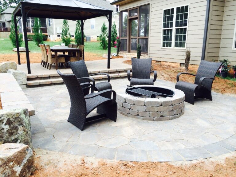 Flagstone-style paver patio with a stone fire pit, wicker seating and steps up to a covered dining area