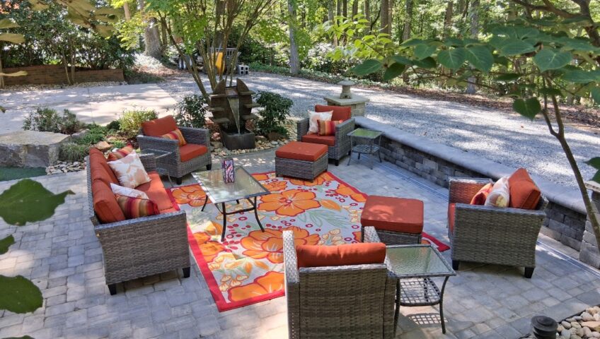 Paver patio with a block seating wall, fountain feature and outdoor lounge furniture under shade trees