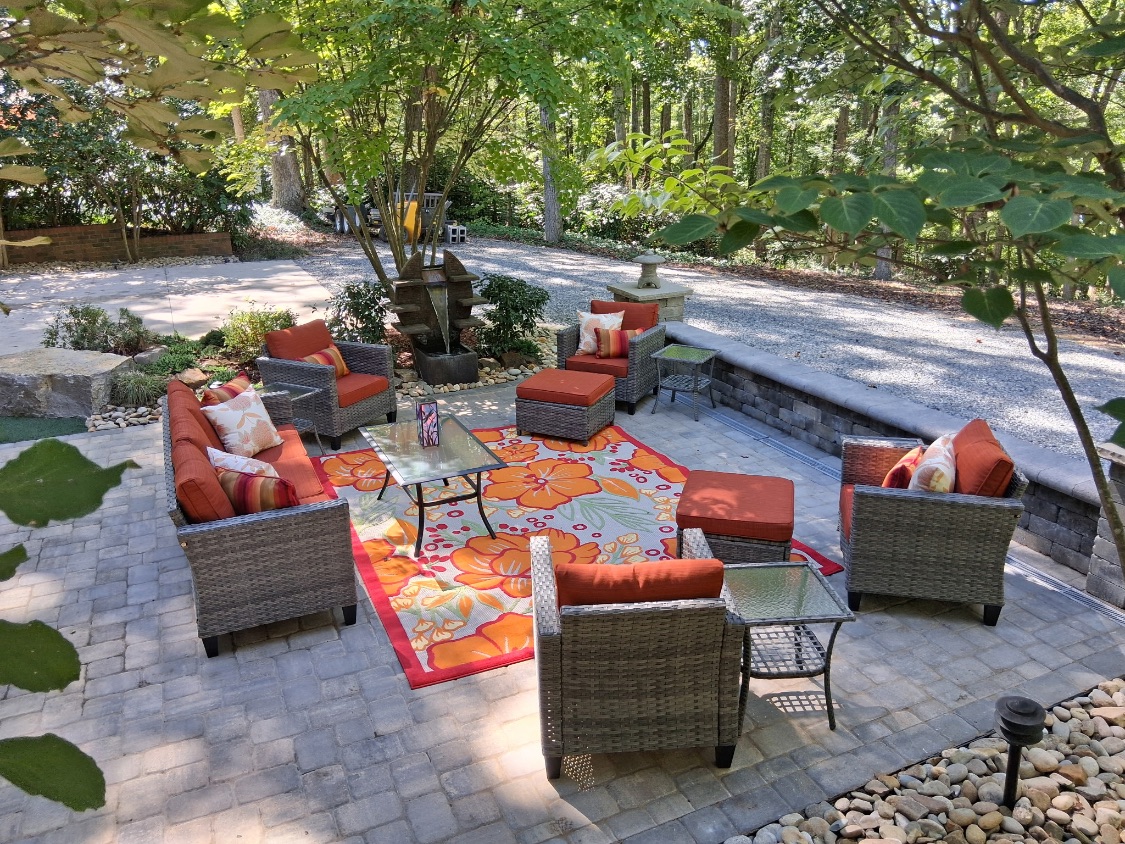 Paver patio with a block seating wall, fountain feature and outdoor lounge furniture under shade trees