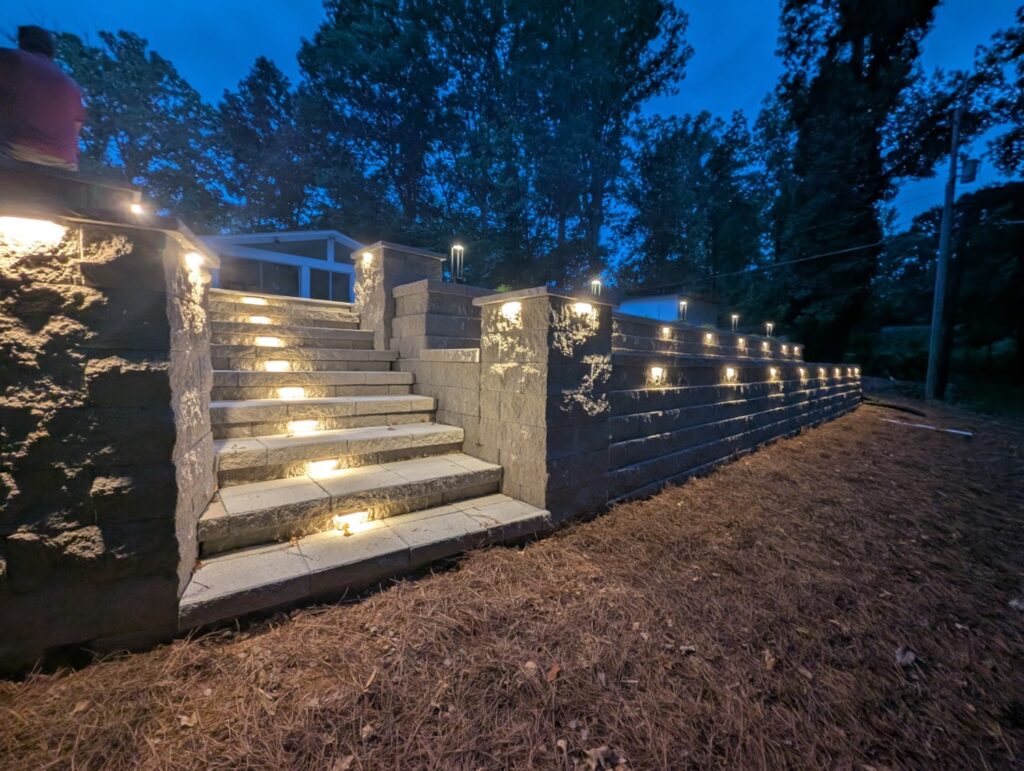 Retaining Walls 101: When You Need One and How They’re Built to Last 2 Segmental block retaining wall and stone steps with built-in step and wall cap lighting at dusk