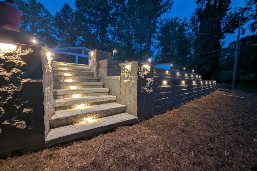 Segmental block retaining wall and stone steps with built-in step and wall cap lighting at dusk