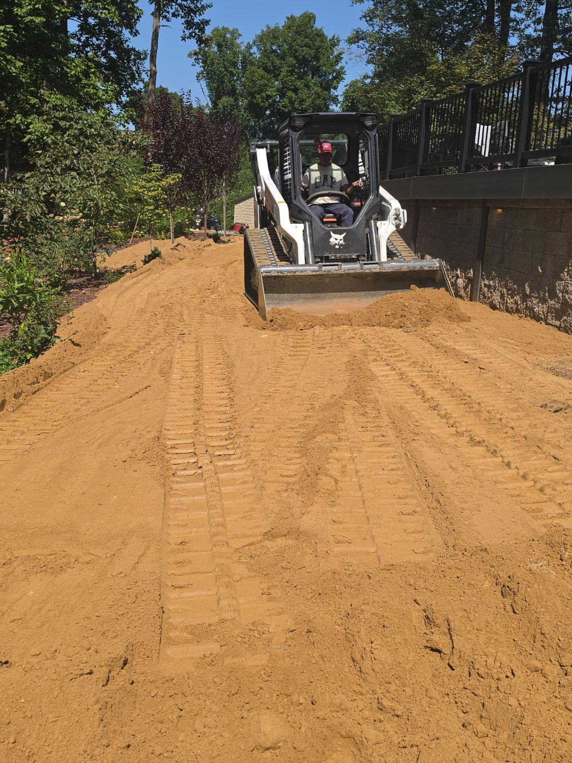 Bobcat track loader grading soil along a retaining wall