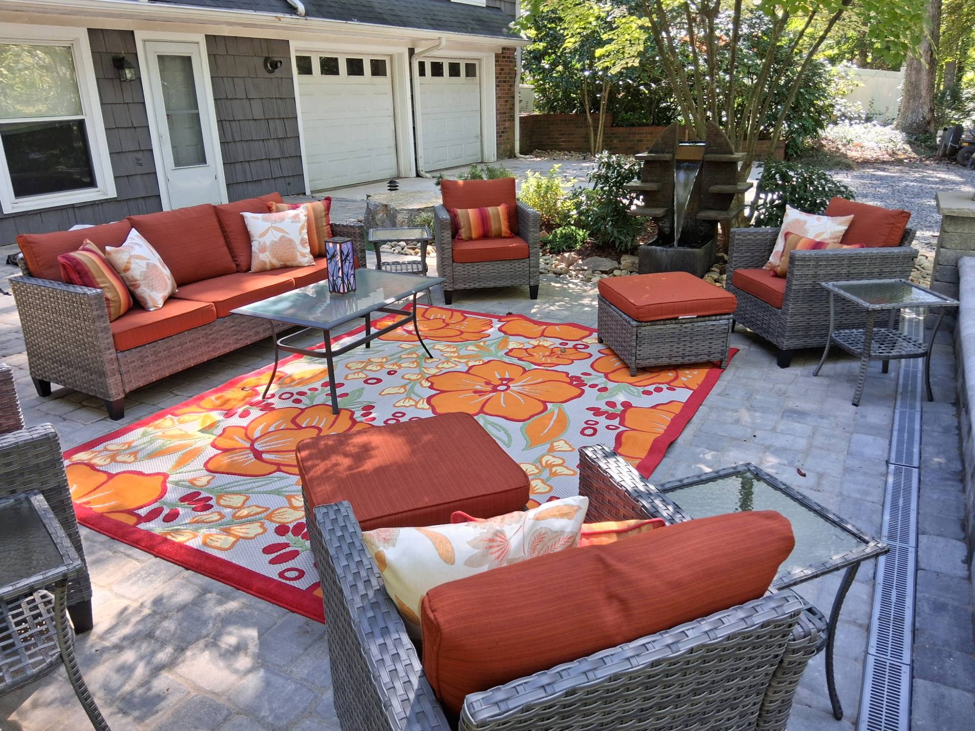 Paver patio outdoor living space with wicker seating, outdoor rug, and stone water fountain