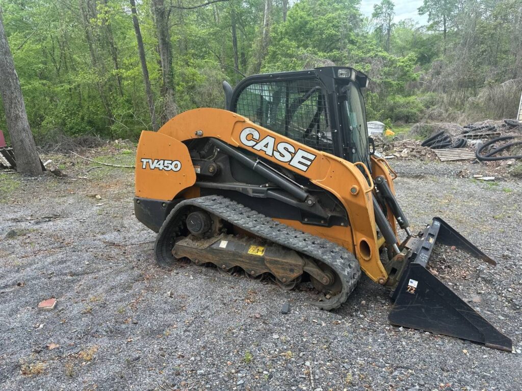 CASE TV450 compact track loader with a cab and a 72-inch bucket, parked on gravel beside woods