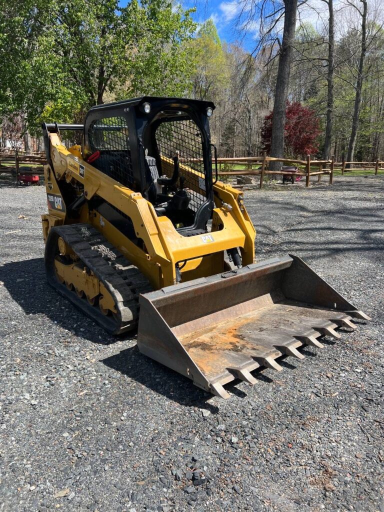 CAT 259D compact track loader with a toothed bucket on a gravel drive beside a split-rail fence