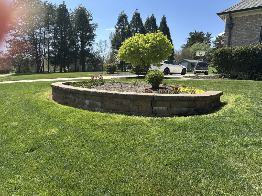 Curved segmental block retaining wall around a raised planting bed in Colfax, NC by Garrison's Landscaping
