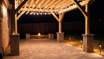 Cedar pergola with string lights and stone pillars over paver patio at night — Garrison Landscaping